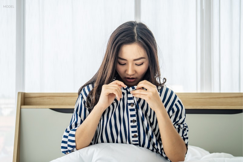 Unhappy women looking down her shirt at her breasts, unhappy with their size.