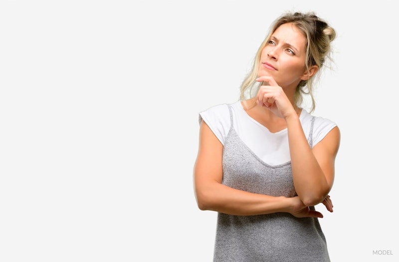 Woman with hand on chin, contemplating a decision like plastic surgery.