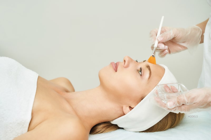 Woman getting a chemical peel with her aesthetician brushing solution on her forehead.