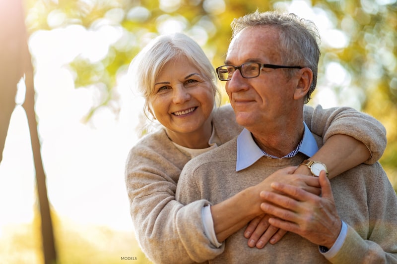 Happy, mature couple embracing outdoors, surrounded by trees.