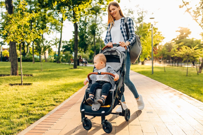 Attractive woman pushing a toddler in a stroller through the park.